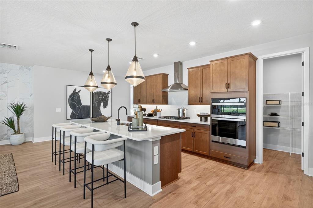 A modern kitchen features wood cabinets, a white quartz island with bar seating, and stainless appliances — 34890 FLOWER PATCH DRIVE, DADE CITY, FL