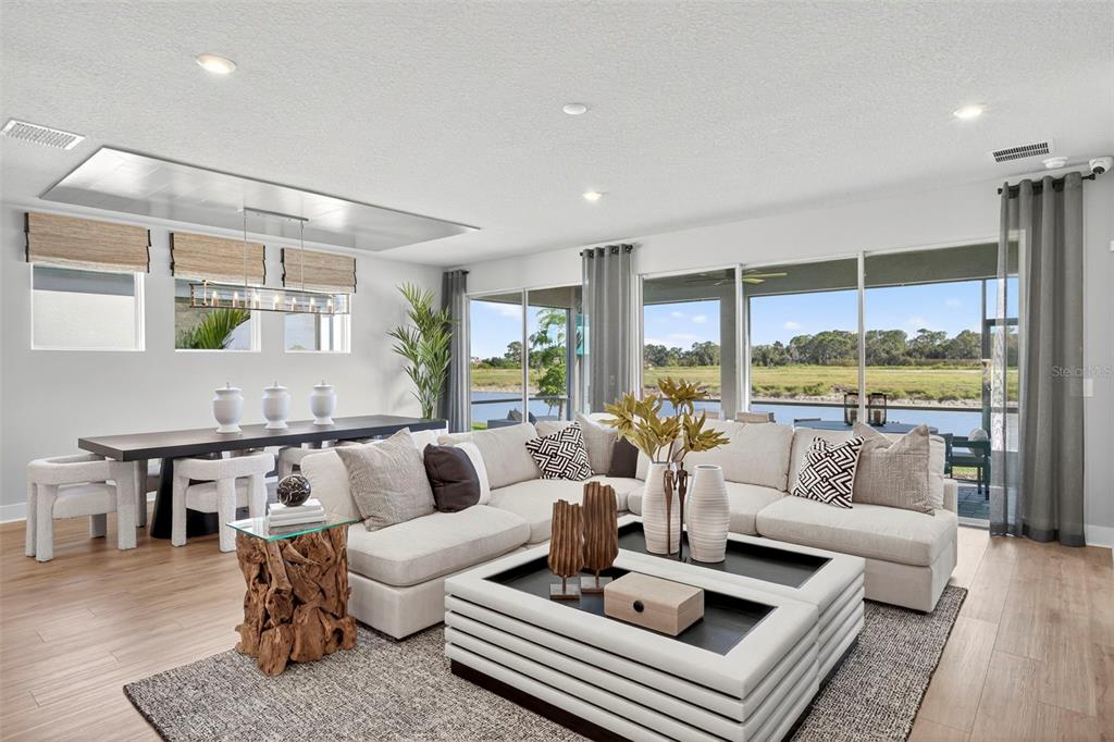A bright living and dining area features a large sectional sofa, wooden table, and water views — 34890 FLOWER PATCH DRIVE, DADE CITY, FL