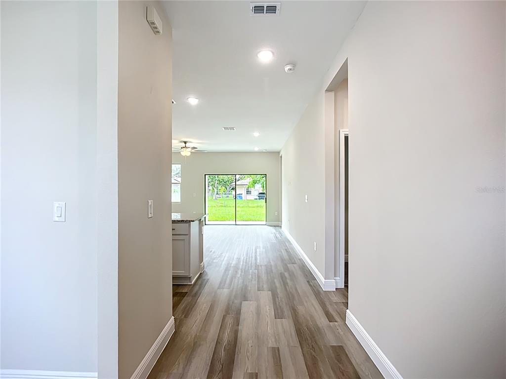 A hallway with wood-look flooring leads to an open kitchen and a sliding glass door — 4446 LARATONDA ROAD, NORTH PORT, FL