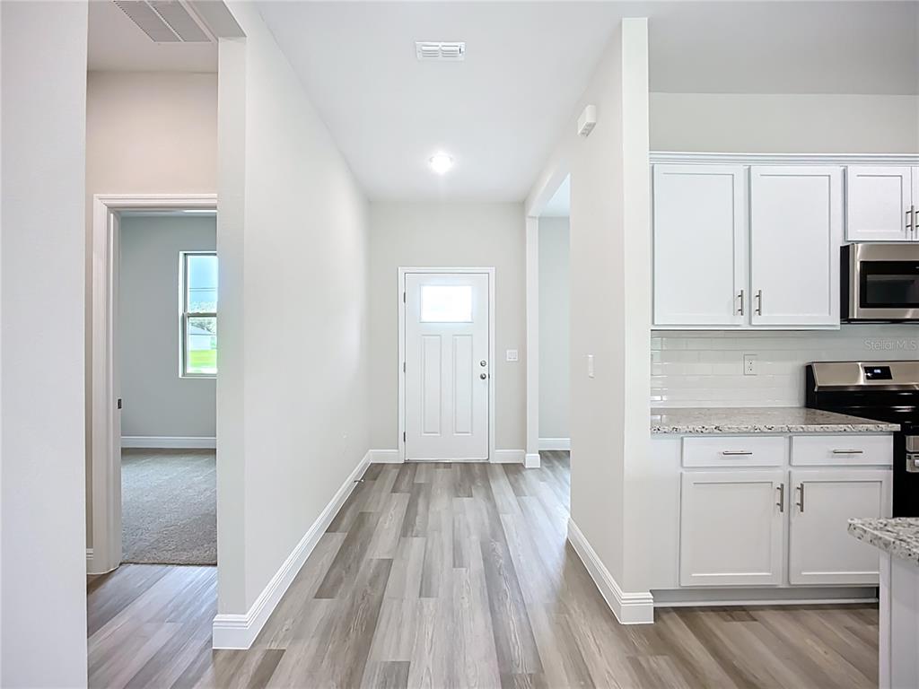 A hallway with wood-look flooring leads to an exterior door, flanked by a kitchen area — 4446 LARATONDA ROAD, NORTH PORT, FL