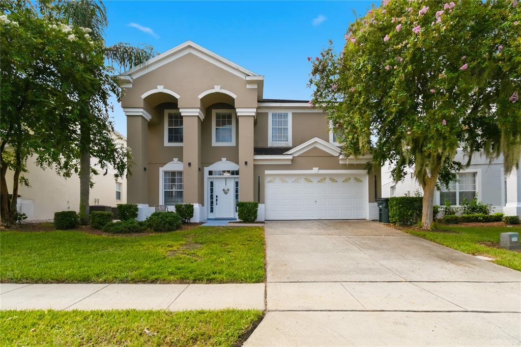 A two-story suburban house with a tan stucco exterior, white trim, and a two-car garage — 8006 KING PALM CIRCLE, KISSIMMEE, FL