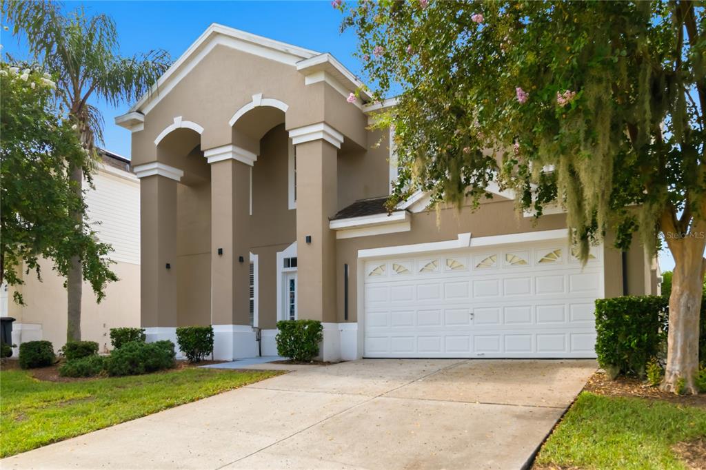 A two-story tan house with a two-car garage and a covered entryway with arched columns — 8006 KING PALM CIRCLE, KISSIMMEE, FL