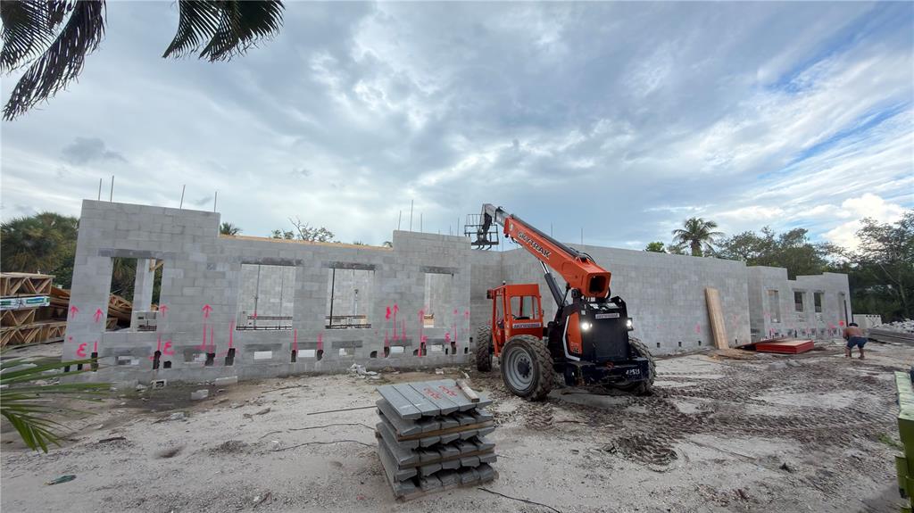 A construction site features a concrete block wall and an orange telehandler under a cloudy sky — 546 FREELING DRIVE, SARASOTA, FL