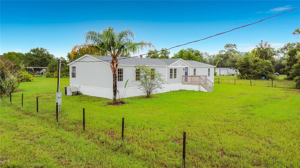 A light-colored manufactured home sits on a grassy lot with a palm tree and fence — 9200 MERCURY DRIVE, ST CLOUD, FL
