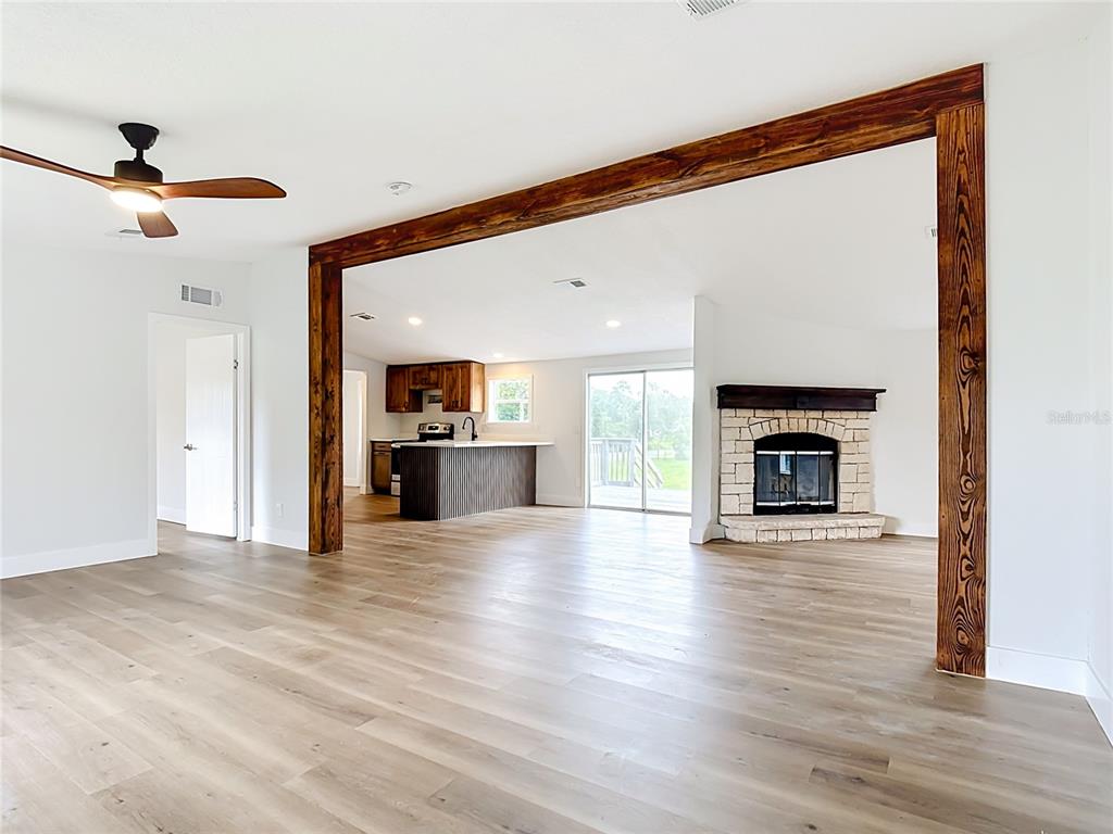 An open-concept living area features light wood flooring, a stone fireplace, and a wooden beam — 9200 MERCURY DRIVE, ST CLOUD, FL