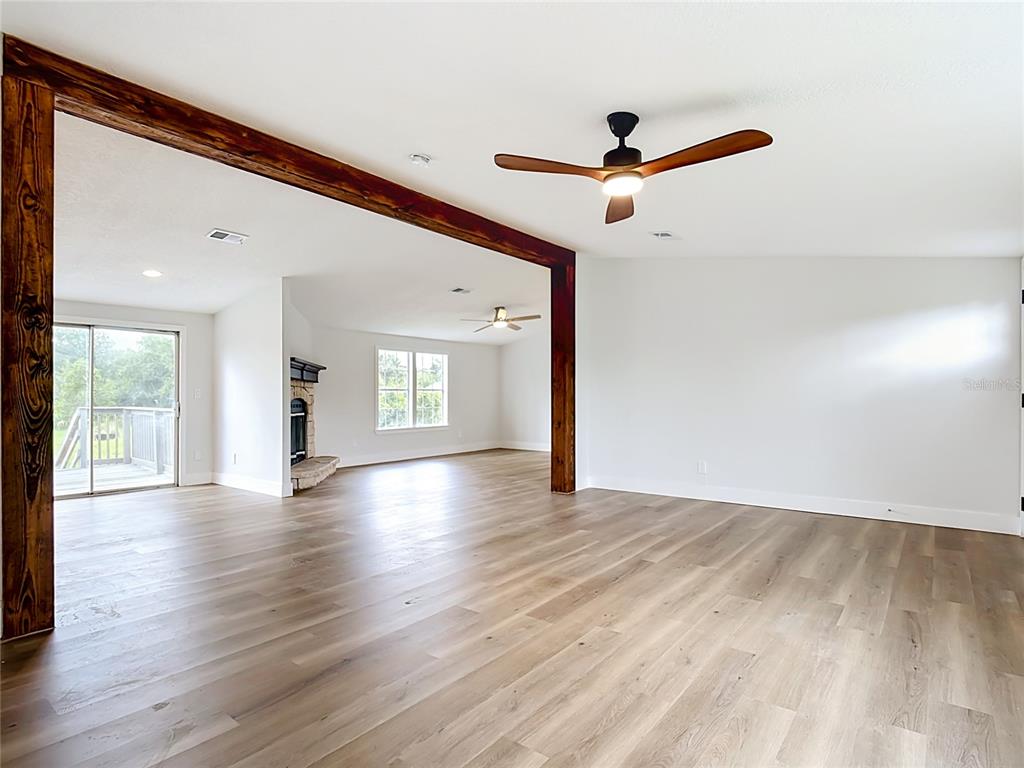 An open living area features light wood flooring, a large wooden beam, and a ceiling fan — 9200 MERCURY DRIVE, ST CLOUD, FL