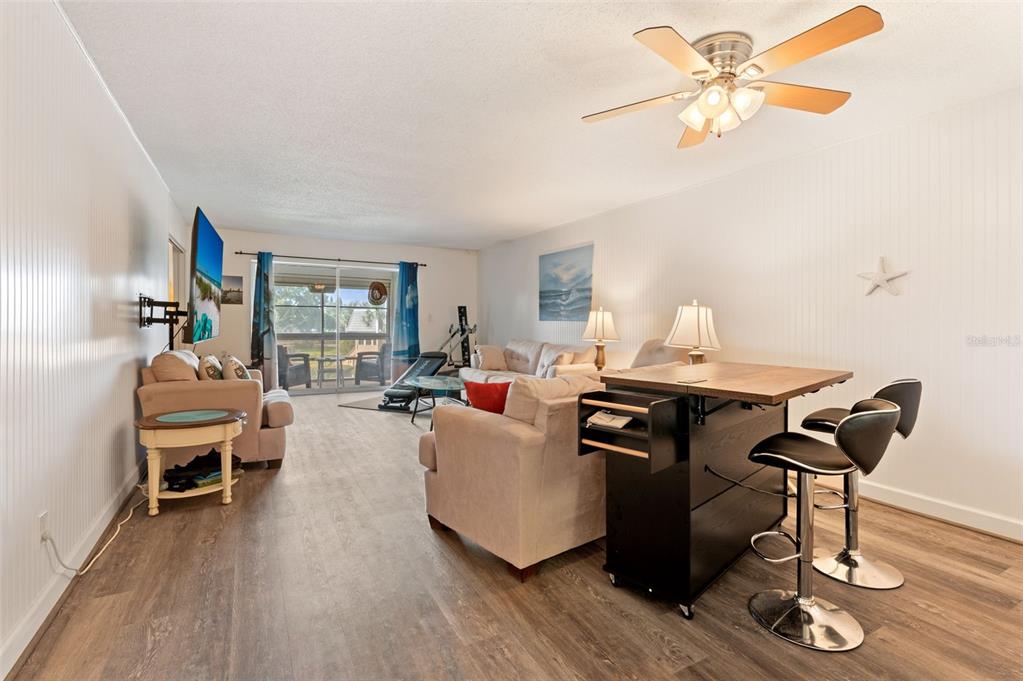 A living room features light wood-look flooring, a ceiling fan, and a kitchen island with stools — 719 CORDOVA GREEN UNIT 719, SEMINOLE, FL