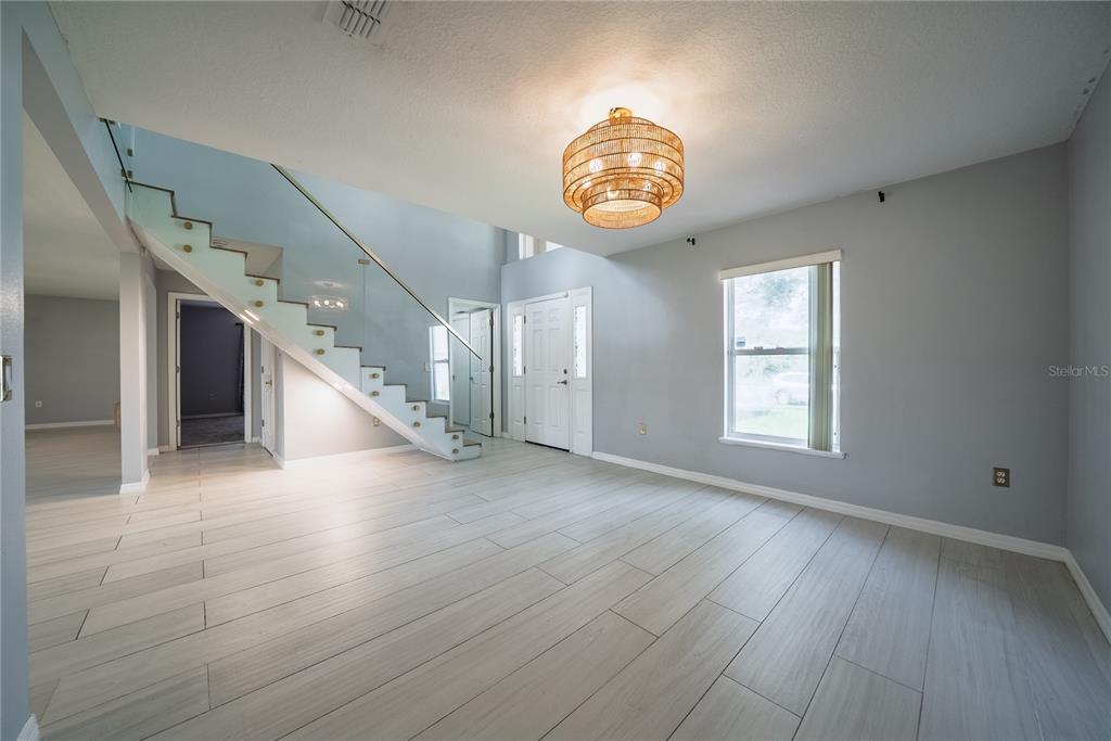 A bright entryway features light wood-look tile flooring, a glass-railed staircase, and a woven chandelier — 3209 ROMAINE COURT, ORLANDO, FL