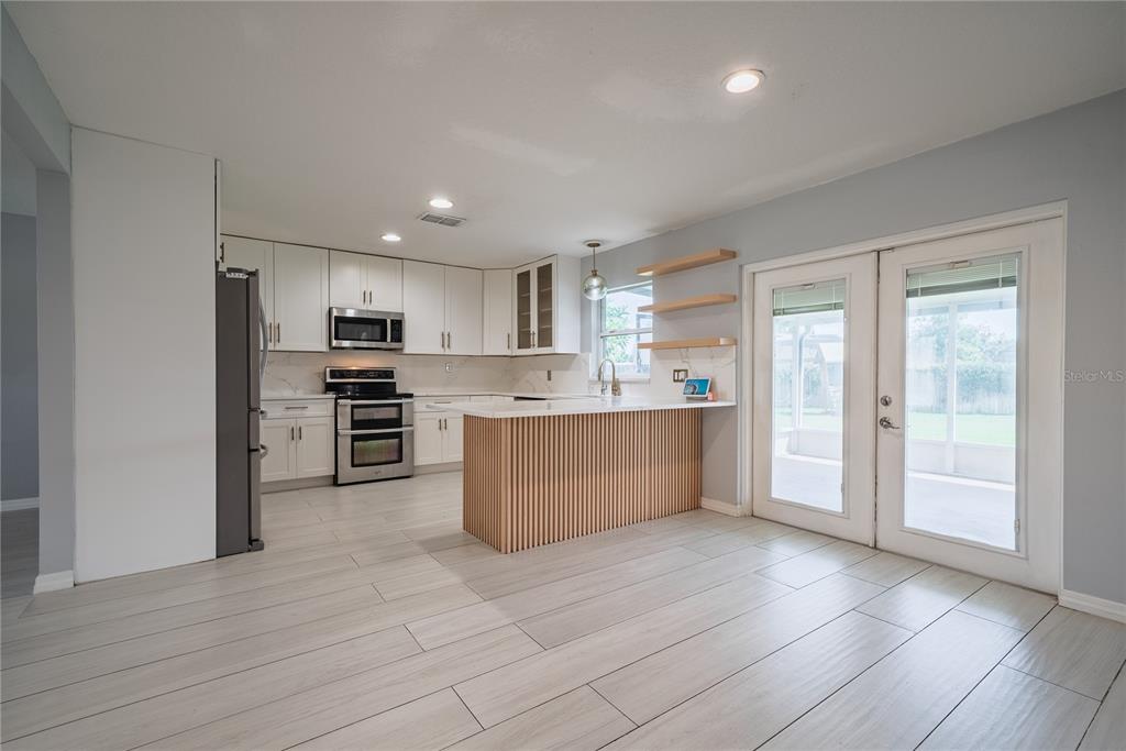 A modern kitchen features white cabinets, a slatted wood island, and light-colored tile flooring — 3209 ROMAINE COURT, ORLANDO, FL