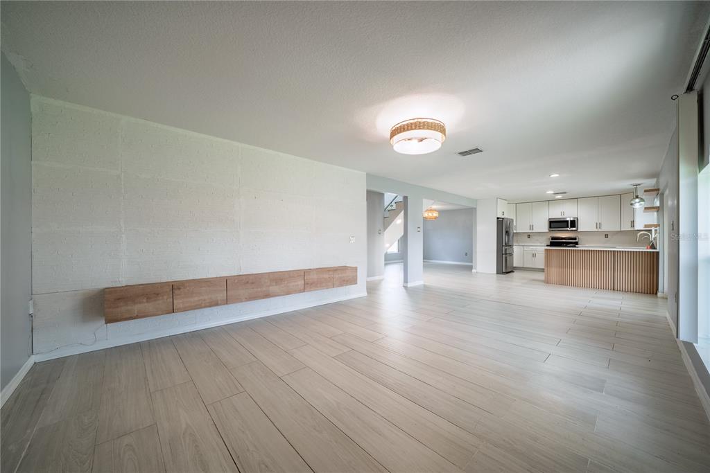 An open-concept living area features light wood-look tile flooring, a white brick wall, and a kitchen — 3209 ROMAINE COURT, ORLANDO, FL