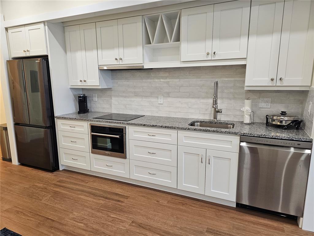 A modern kitchen features white cabinets, granite countertops, stainless steel appliances, and wood-look flooring — 51 MAC EWEN DRIVE UNIT 14, OSPREY, FL