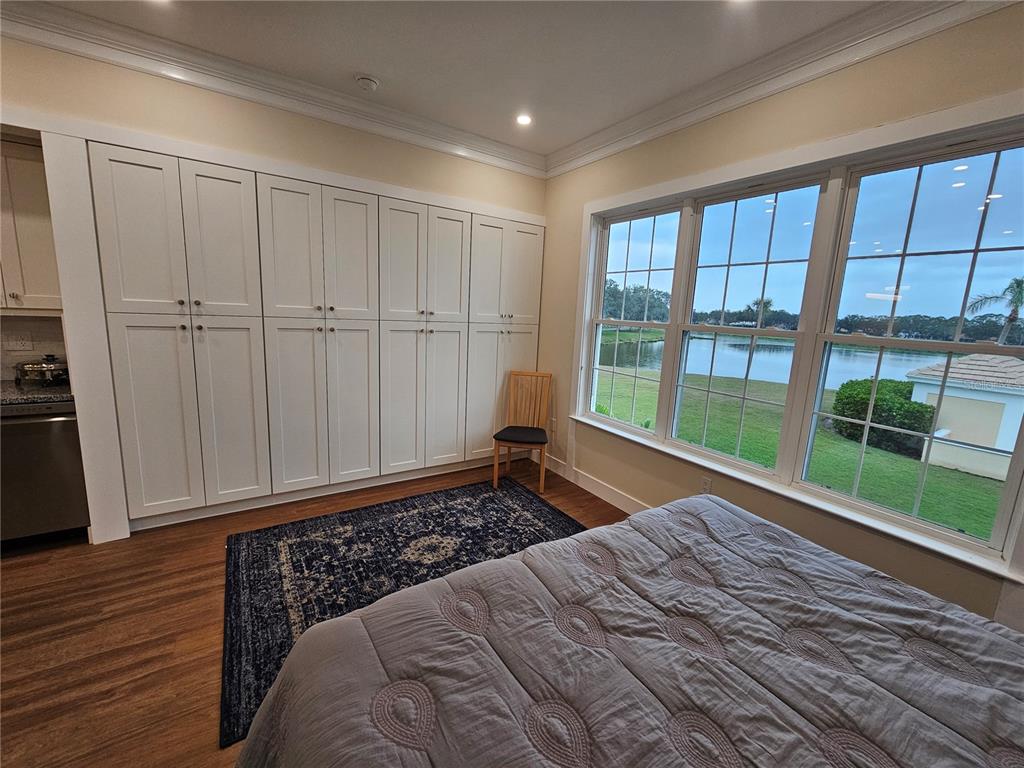 A bedroom features white built-in cabinets, a patterned rug, and large windows overlooking a lake — 51 MAC EWEN DRIVE UNIT 14, OSPREY, FL
