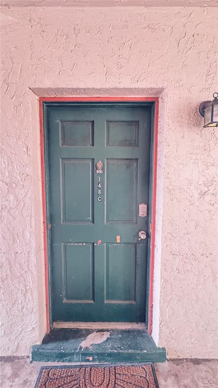 A green front door with the number 148C is set into a textured, light-colored exterior wall — 4315 AEGEAN DRIVE UNIT 148C, TAMPA, FL
