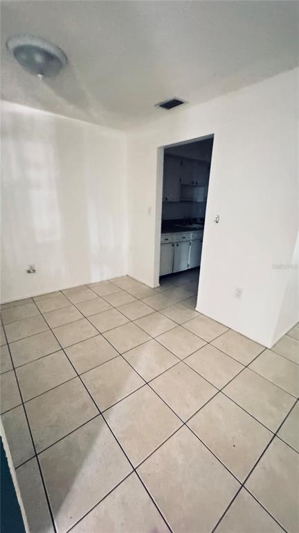 A room with light-colored tile flooring leads into a kitchen with white cabinets — 4315 AEGEAN DRIVE UNIT 148C, TAMPA, FL