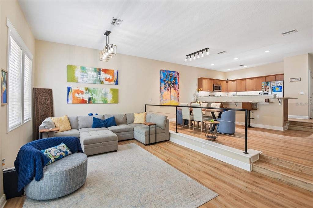 A living room features light wood flooring, a gray sectional sofa, and two modern chandeliers — 131 ATHENIAN WAY, TARPON SPRINGS, FL