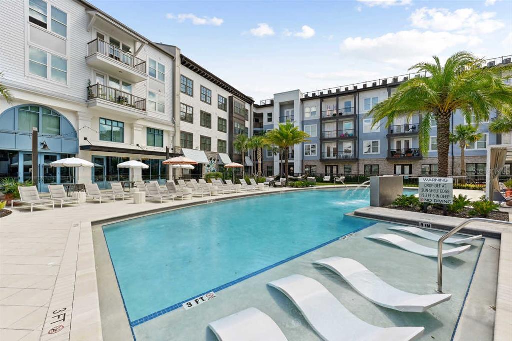 An outdoor swimming pool with a sun shelf and lounge chairs sits between apartment buildings — 1464 LAUREL SOUND LANE UNIT C1, SANFORD, FL