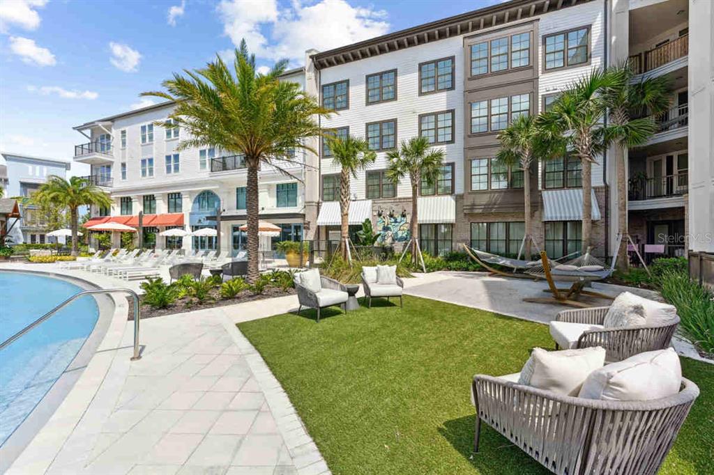 A swimming pool area features lounge chairs, palm trees, and outdoor seating on a lawn — 1464 LAUREL SOUND LANE UNIT C1, SANFORD, FL