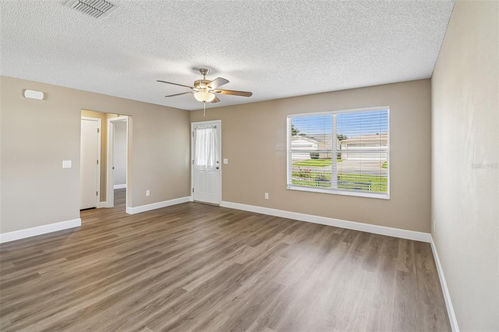 An empty living room with light brown walls, wood-look flooring, a ceiling fan, and window — 2609 PRIVADA DRIVE, THE VILLAGES, FL