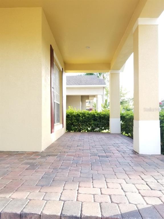 A covered front porch features paver flooring, yellow stucco walls, and a white support column — 13448 ZORI LANE, WINDERMERE, FL
