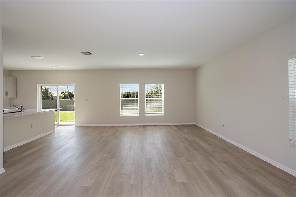 An open-concept living area features light wood-look flooring, neutral walls, and a sliding glass door — 33840 NOBLE CREEK PLACE, DADE CITY, FL