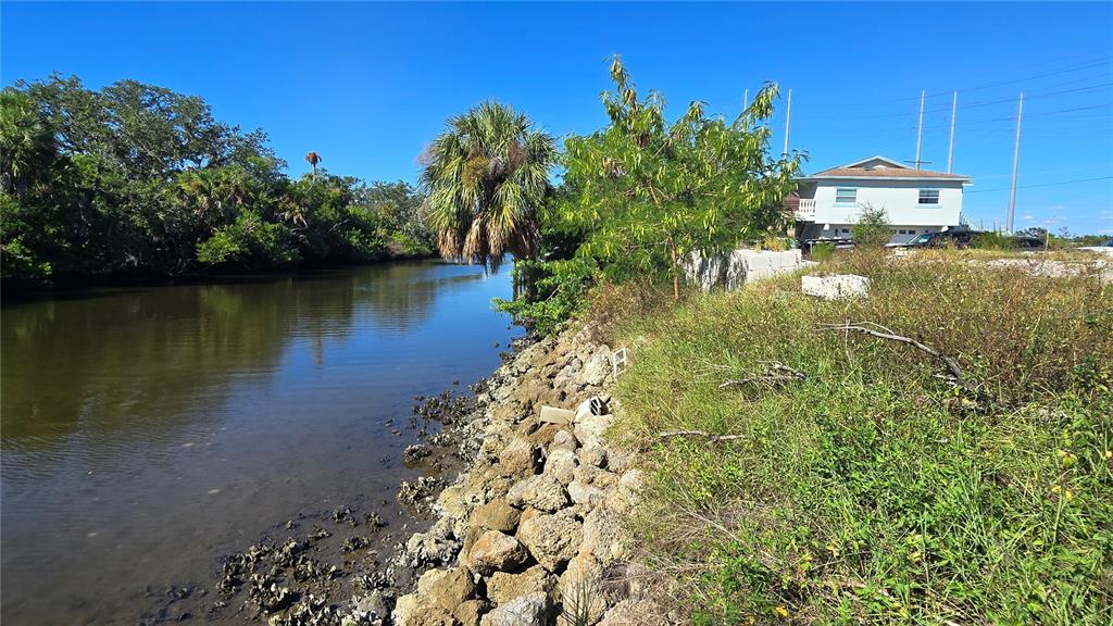 A canal flows alongside a rocky embankment leading to a house in a grassy yard — 9919 BAY DRIVE, GIBSONTON, FL