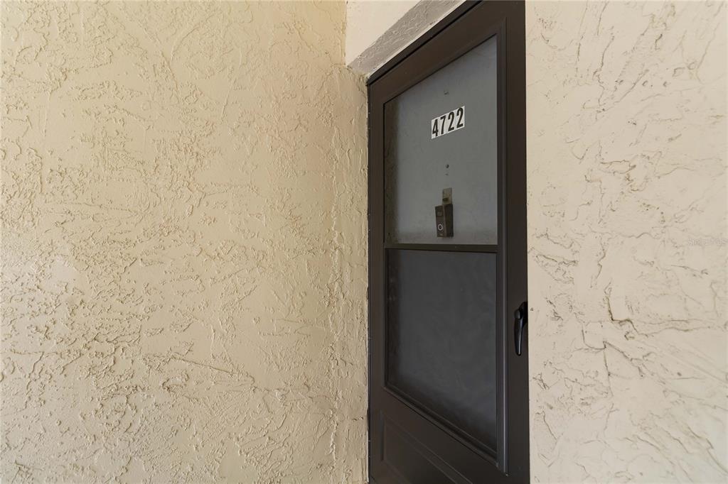 A dark-framed storm door with the number 4722 is set into a textured beige stucco wall — 4722 KILT COURT UNIT 65, ST CLOUD, FL