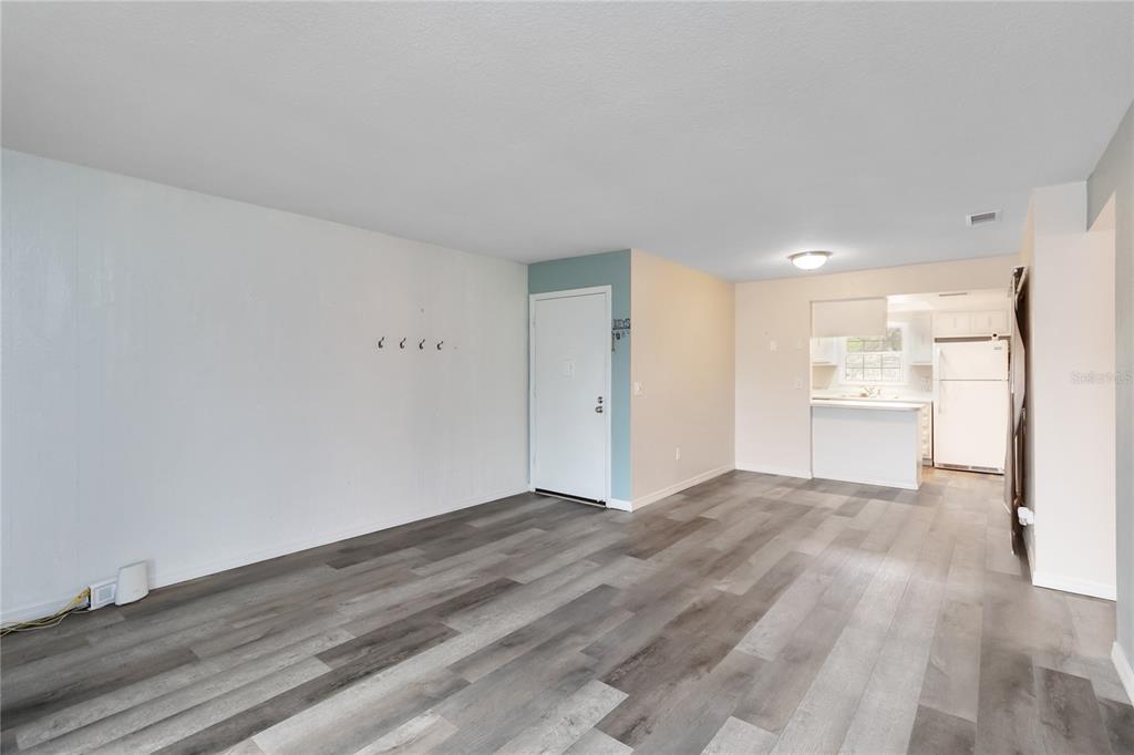 An open-concept living area features gray wood-look flooring, white walls, and an adjacent kitchen — 4722 KILT COURT UNIT 65, ST CLOUD, FL