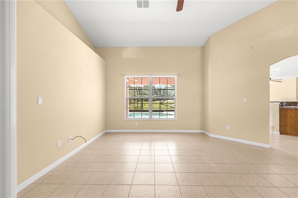 An empty room with beige walls, tile flooring, a vaulted ceiling, and a large window — 4731 SW GARDENIA COURT, DUNNELLON, FL