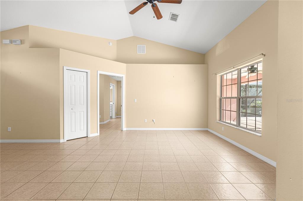 An empty room with beige walls, tile flooring, a vaulted ceiling, and a large window — 4731 SW GARDENIA COURT, DUNNELLON, FL