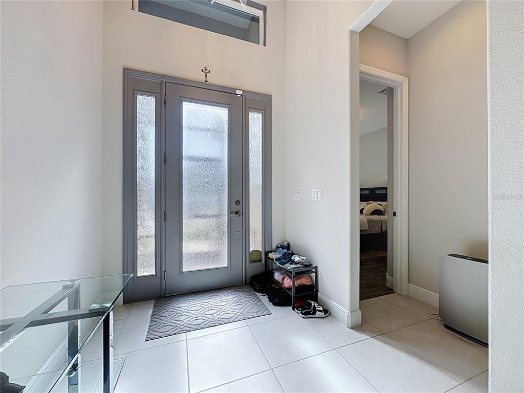 A bright entryway features a gray front door with glass panels and light tile flooring — 8665 E BRIDGEPORT BAY CIRCLE, MOUNT DORA, FL