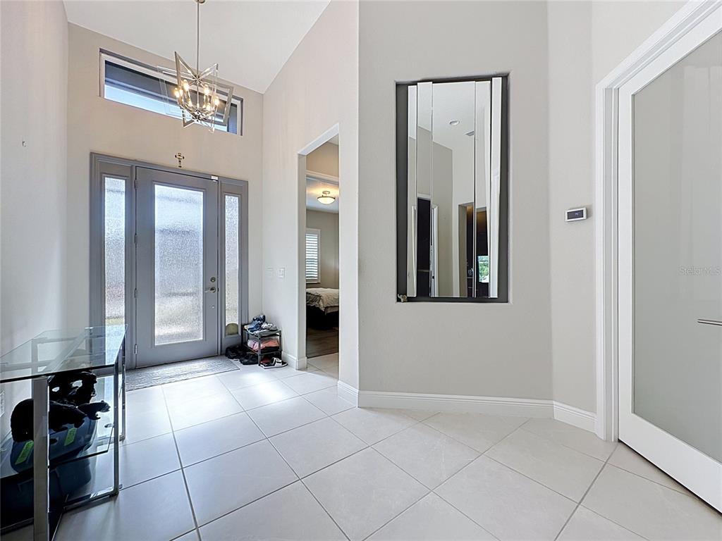 A bright entryway features a glass-paneled front door, tiled floors, and a tall wall mirror — 8665 E BRIDGEPORT BAY CIRCLE, MOUNT DORA, FL