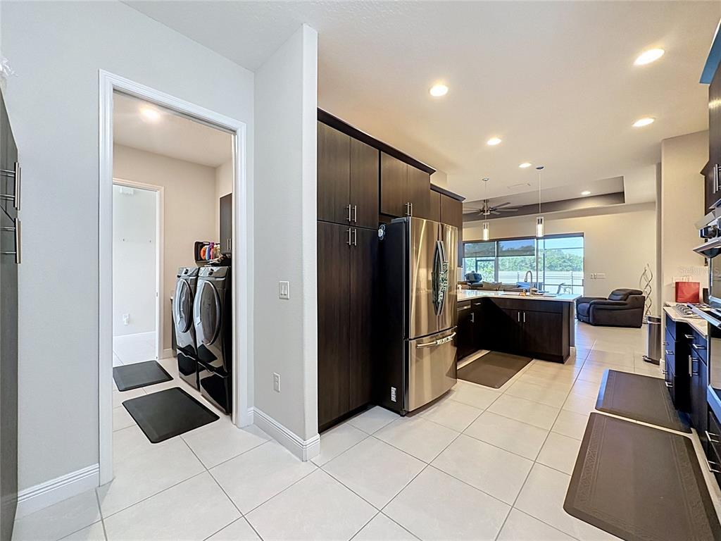 A kitchen with dark cabinets and stainless steel appliances leads into a laundry room — 8665 E BRIDGEPORT BAY CIRCLE, MOUNT DORA, FL