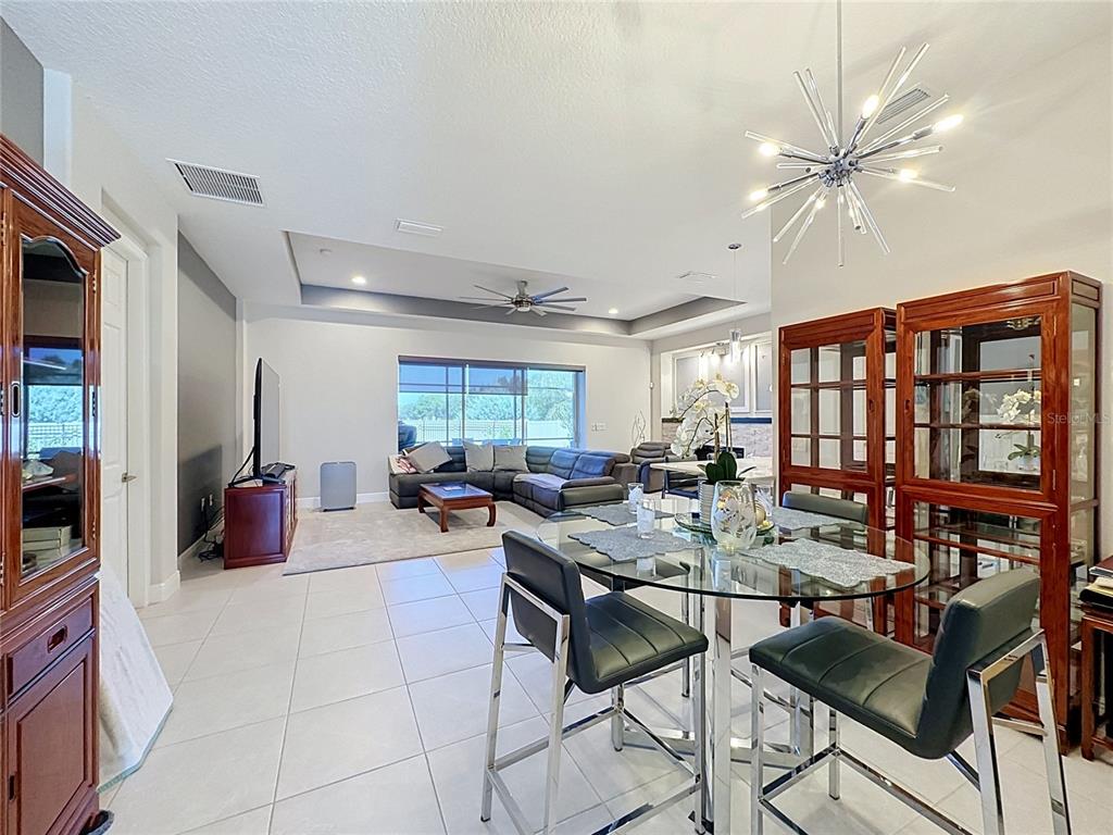 A bright open-concept living and dining area features tile flooring, a tray ceiling, and furniture — 8665 E BRIDGEPORT BAY CIRCLE, MOUNT DORA, FL