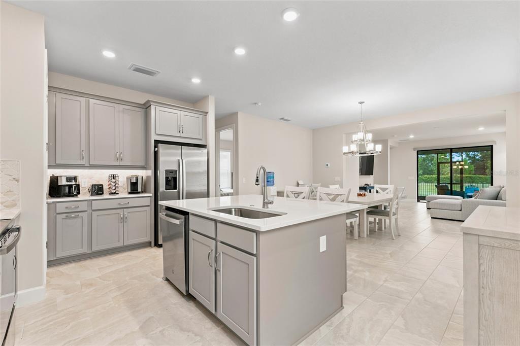 A modern kitchen with gray cabinetry, a central island, and an open-concept dining area — 1389 LAMBARDI COURT, POINCIANA, FL