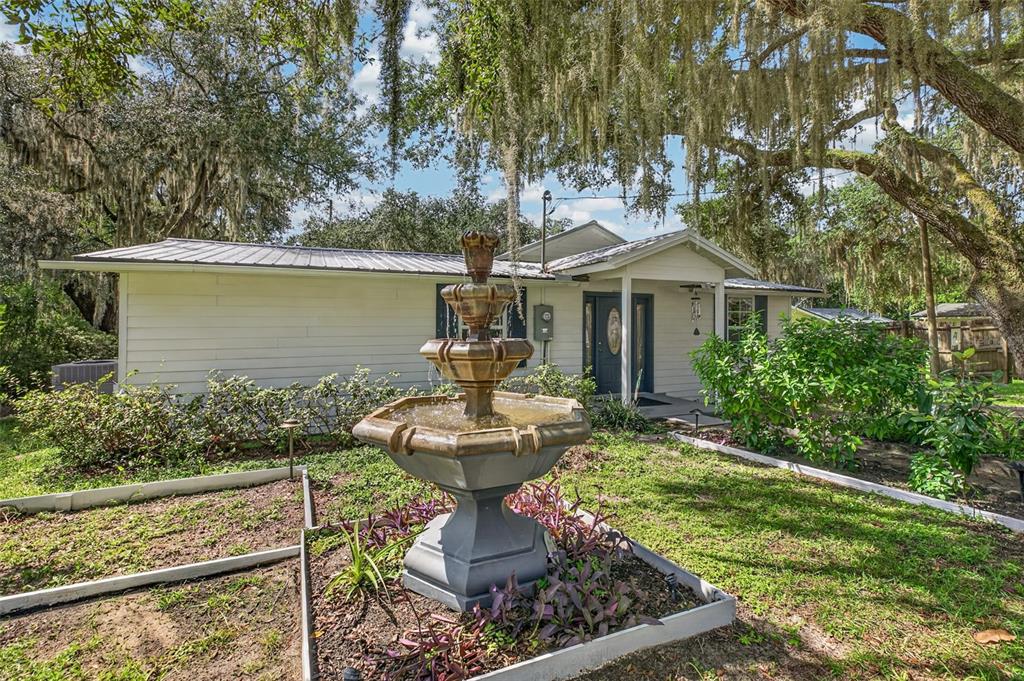 A white house with a metal roof features a tiered fountain in the front yard — 5927 WHITE SANDS ROAD, KEYSTONE HEIGHTS, FL
