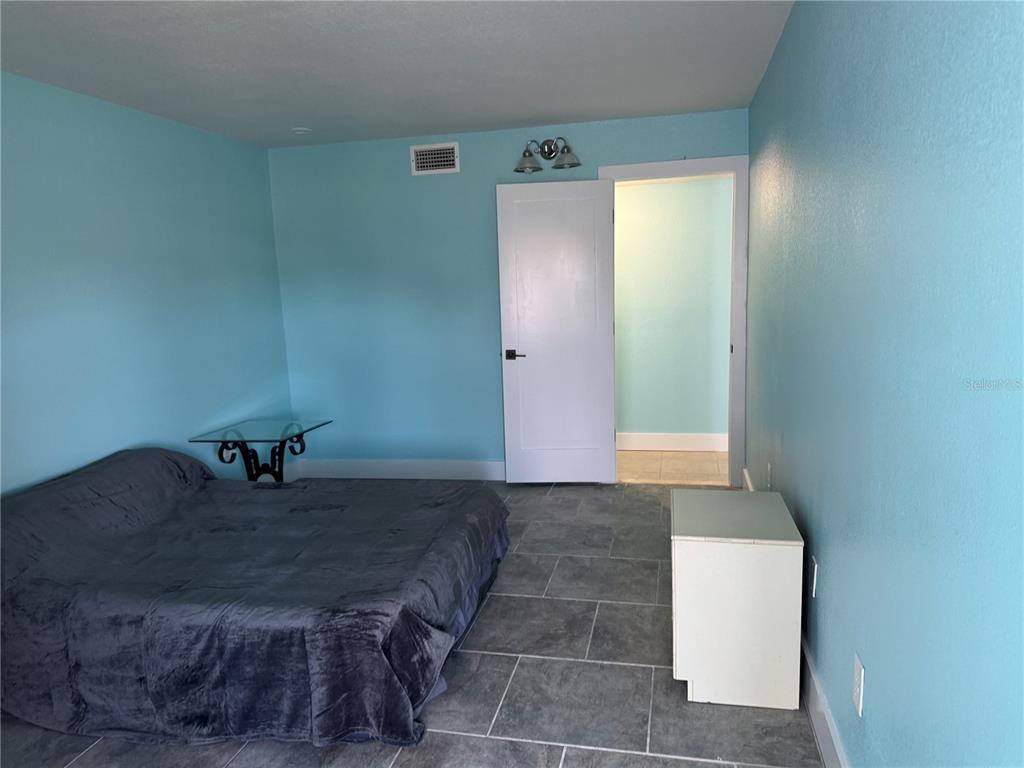 A bedroom with light blue walls, gray tile flooring, a bed, and an open doorway — 4515` MARINE PARKWAY UNIT 102, NEW PORT RICHEY, FL