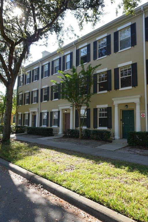 A three-story townhouse exterior with tan siding, black shutters, and a sidewalk in front — 1004 WATERSIDE DRIVE UNIT 1004, CELEBRATION, FL