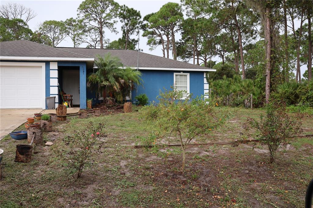 A blue single-story house with a white garage door and a sparse, sandy front yard — 1102 REDBIRD STREET, LAKE PLACID, FL