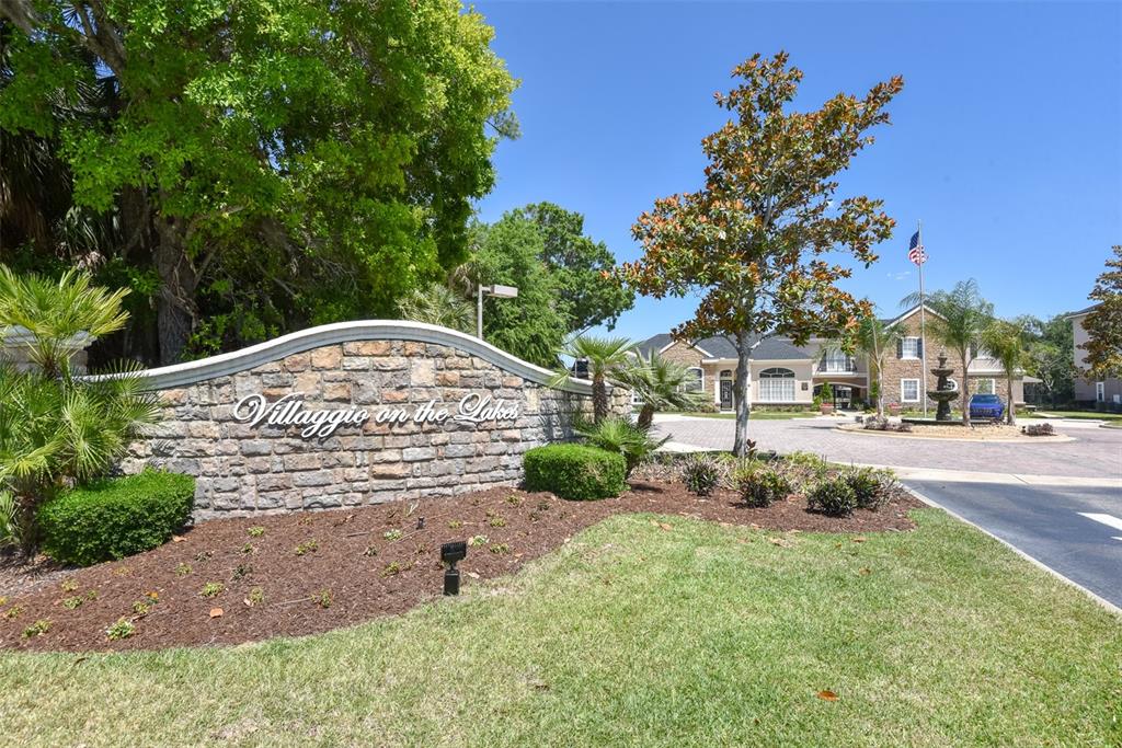 A stone entrance sign for Villaggio on the Lakes stands before a paved roundabout — 940 VILLAGE TRAIL UNIT 6-103, PORT ORANGE, FL