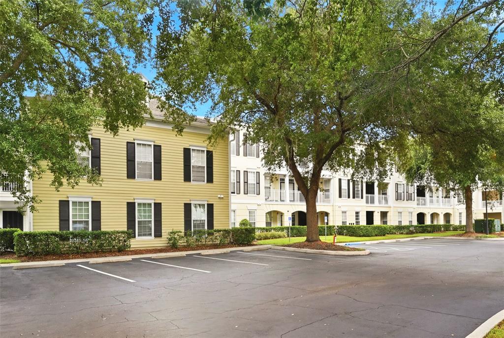 A yellow multi-story apartment building with black shutters stands behind a paved parking lot — 239 LONGVIEW AVENUE UNIT 207, CELEBRATION, FL