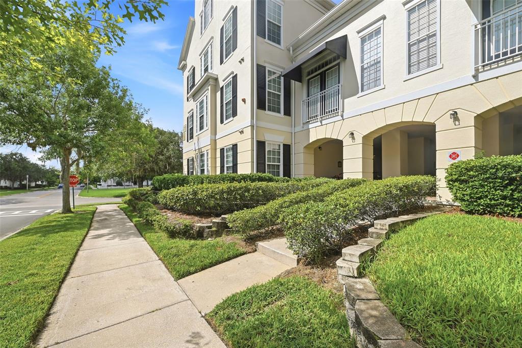 A multi-story apartment building exterior features a concrete sidewalk, manicured hedges, and arched entryways — 239 LONGVIEW AVENUE UNIT 207, CELEBRATION, FL