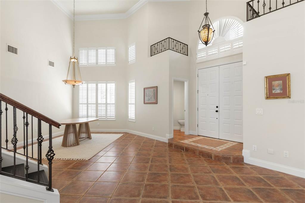 A high-ceilinged foyer features tile flooring, a staircase with iron railings, and a dining area — 6 MONTERREY DRIVE, PALM COAST, FL
