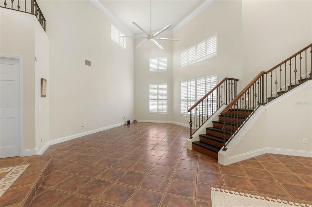 A high-ceilinged room features tile flooring, a staircase with a metal railing, and large windows — 6 MONTERREY DRIVE, PALM COAST, FL