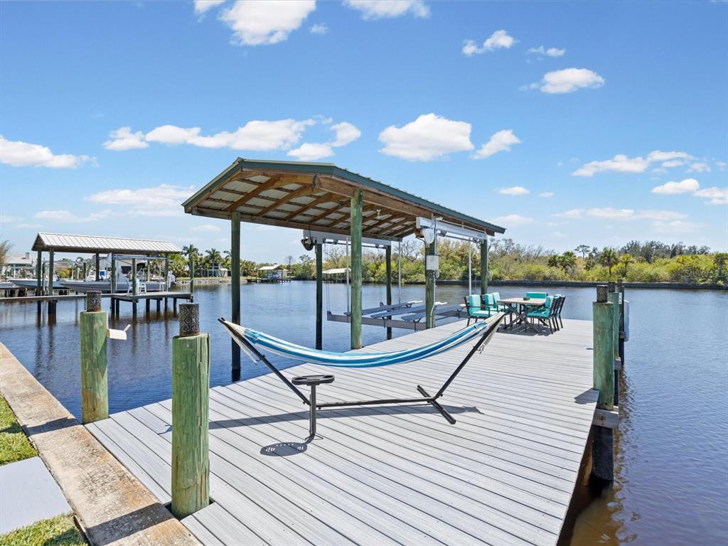 A wooden dock features a hammock, a covered boat slip, and outdoor dining furniture — 1414 DEIRDRE DRIVE, RUSKIN, FL