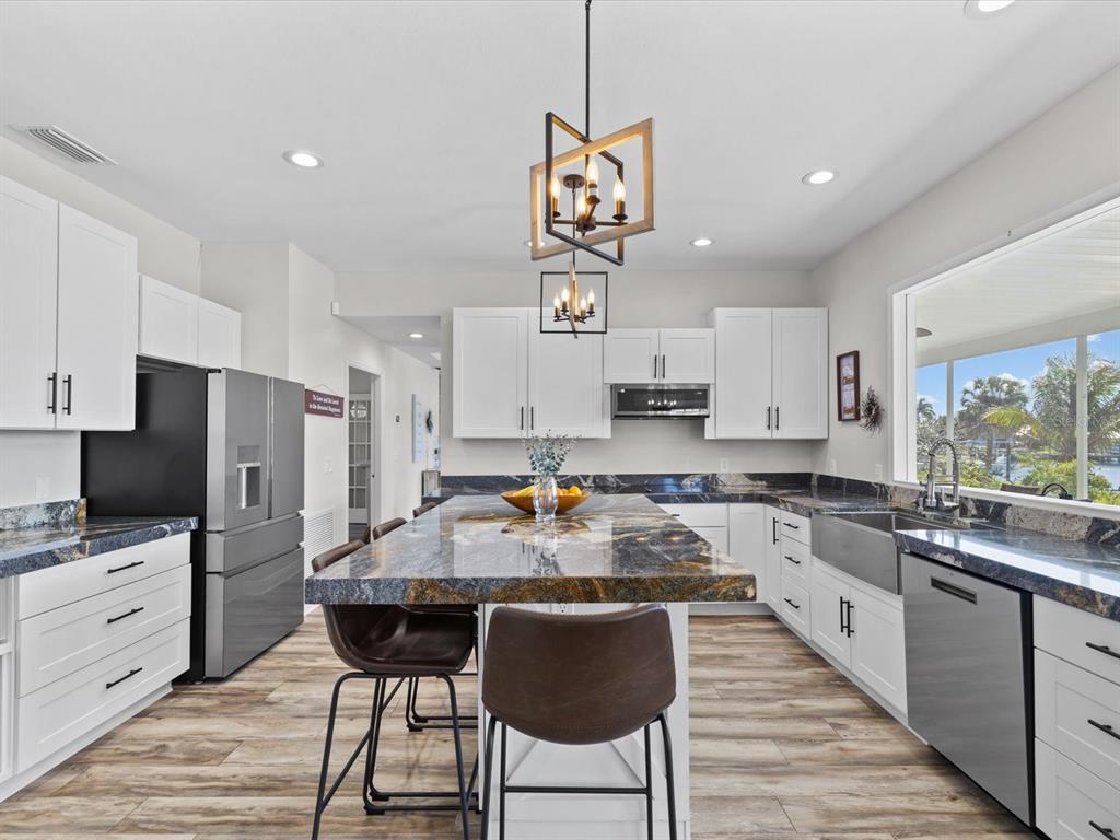 A modern kitchen features white cabinets, dark granite countertops, a large island, and stainless appliances — 1414 DEIRDRE DRIVE, RUSKIN, FL