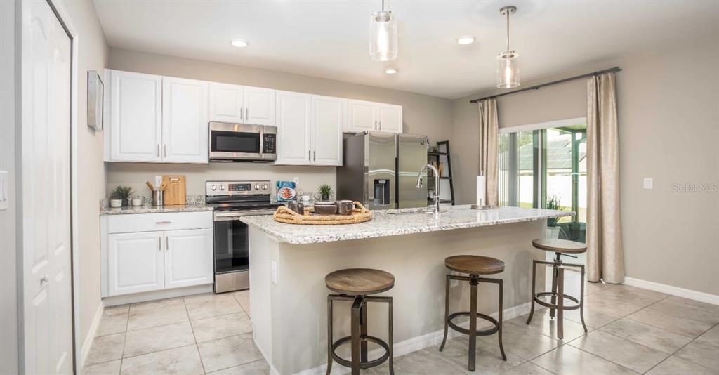 A kitchen features white cabinets, granite countertops, a center island with stools, and stainless appliances — 20431 STARDUST AVENUE, PORT CHARLOTTE, FL