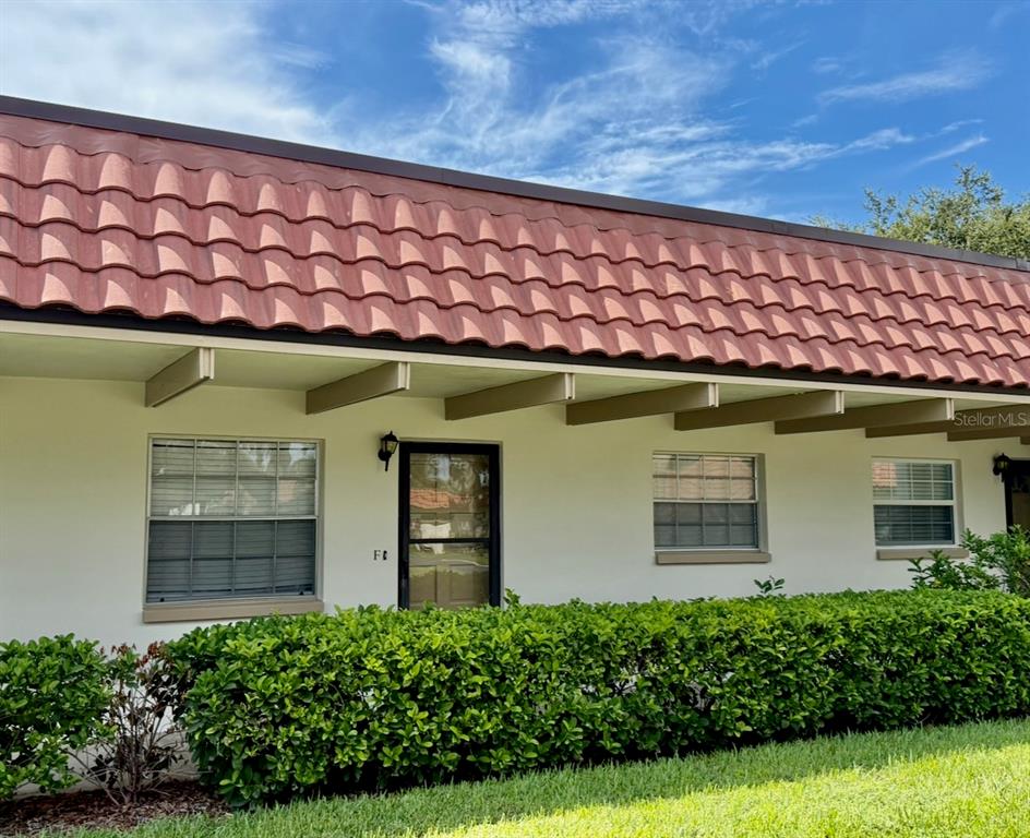 A single-story building exterior features a red tile mansard roof and a manicured hedge — 1701 PINEHURST ROAD UNIT 2F, DUNEDIN, FL