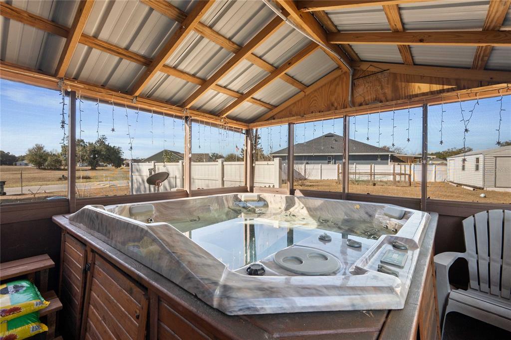 A hot tub sits inside a screened-in porch with a metal roof and wooden framing — 2644 SE 75TH BOULEVARD, BUSHNELL, FL