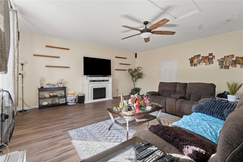 A living room features wood-look flooring, a fireplace with a television, and a ceiling fan — 2644 SE 75TH BOULEVARD, BUSHNELL, FL