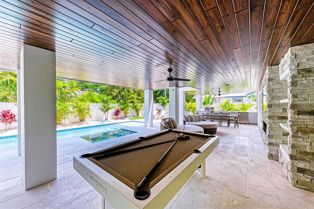 A covered outdoor patio features a pool table, stone fireplace, dining area, and swimming pool — 215 83RD STREET, HOLMES BEACH, FL